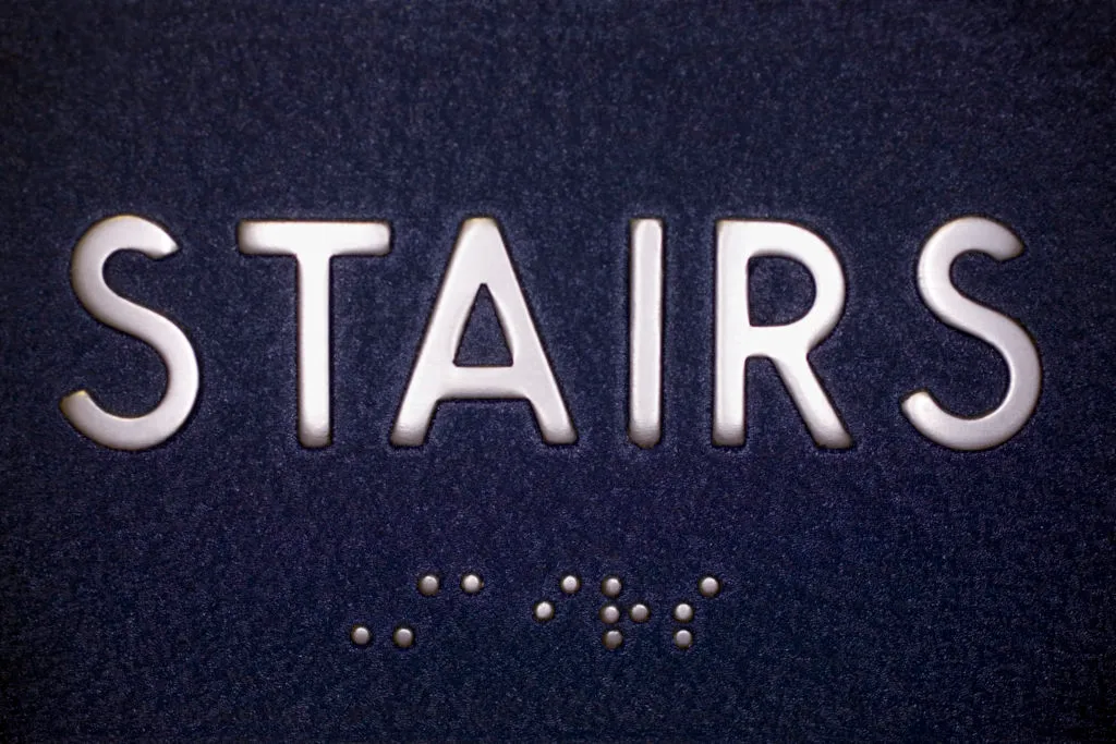 ADA signage displaying the word 'STAIRS' in raised tactile lettering, providing navigation assistance for visually impaired individuals