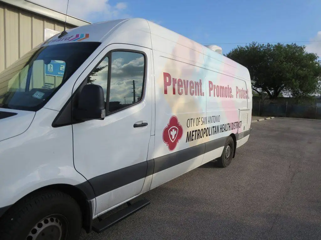 White van from City of San Antonio Metropolitan Health District with health slogans, parked outdoors.