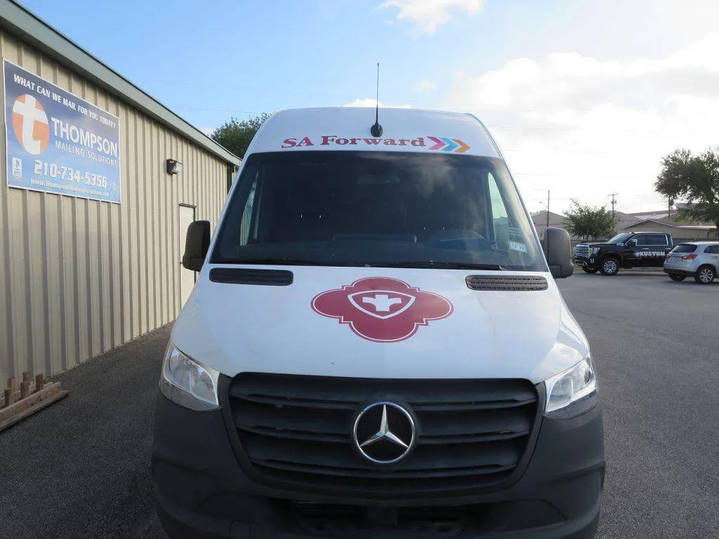 White Mercedes van with a medical logo, likely used for healthcare services or emergencies, parked outdoors.